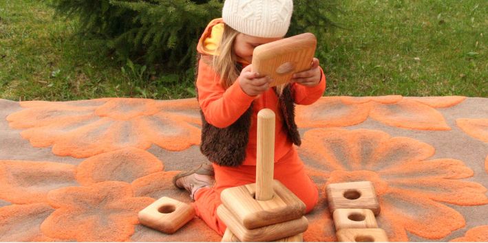 A young girl joyfully stacking wooden blocks on a colorful blanket, showcasing her creativity and playfulness.