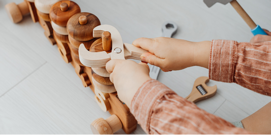 young child is immersed in play with various wooden toys scattered across a smooth wooden floor, highlighting innocence and imagination.