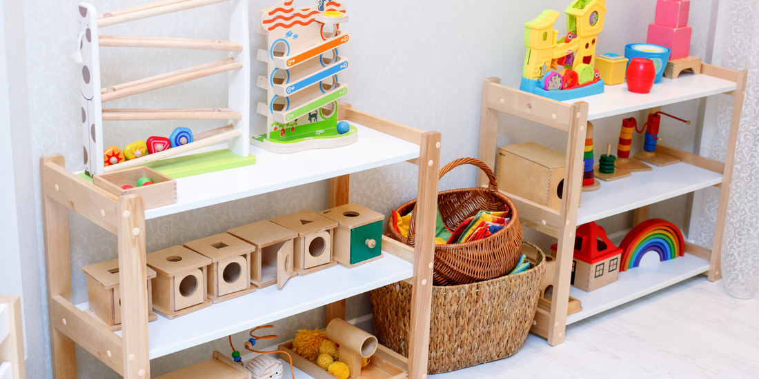 Wooden shelves hold colorful wooden toys, including a marble run, stacking cups, wooden blocks, and puzzle boxes, in a brightly lit children's playroom.