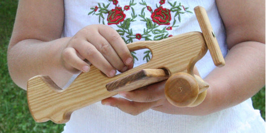 A young girl joyfully holds a wooden airplane toy, showcasing her imagination and playfulness.