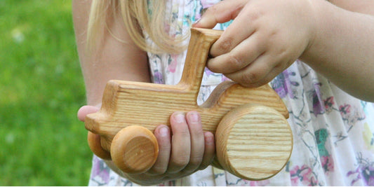 A kid holds a wooden toy tractor, showcasing her playful spirit and imagination.