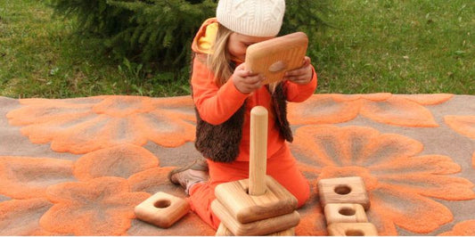 A young girl joyfully stacking wooden blocks on a colorful blanket, showcasing her creativity and playfulness.